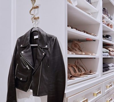 Black leather jacket hanging from cobra-shaped wall hook next to built-in shoe storage shelves in bright white.