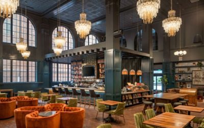 High-ceilinged dining area and bar with several glass chandeliers, rust and olive-colored upholstered dining chairs in different styles.
