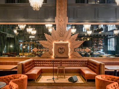 Stage area of dining room surrounded by leather banquette seating in front of mirrored wall with carved decorative focal point.