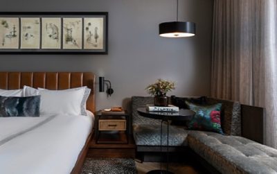 A king bed with cognac leather headboard and plush lounge in dark gray in a guest room of the Thompson Savannah.