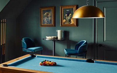 A stylish residential recreation room color-drenched in Pewter Green by Sherwin-Williams, featuring a sofa, billiard table, and antique brass decorative elements.