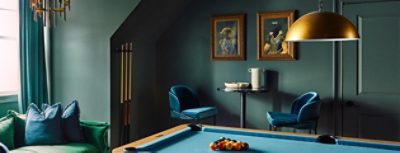 A stylish residential recreation room color-drenched in Pewter Green by Sherwin-Williams, featuring a sofa, billiard table, and antique brass decorative elements.