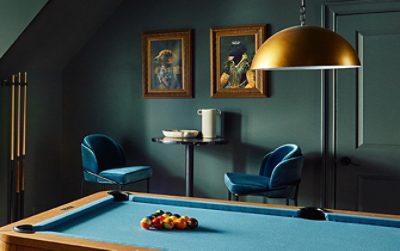A stylish residential recreation room color-drenched in Pewter Green by Sherwin-Williams, featuring a sofa, billiard table, and antique brass decorative elements.