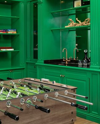 Game room with built-in bookshelves, millwork, and cabinetry painted Sherwin-Williams Lucky Green, a foosball table, board games, and a wet bar area.