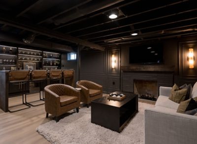 Basement room, color-drenched in Sherwin-Williams Iron Ore, with a home bar, brown leather stools, and a seating area with a sofa and armchairs. 