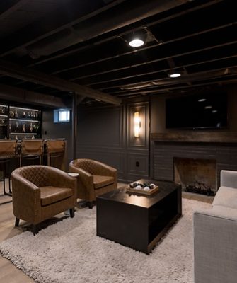 Basement room, color-drenched in Sherwin-Williams Iron Ore, with a home bar, brown leather stools, and a seating area with a sofa and armchairs. 