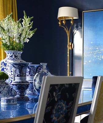 Blue and white porcelain vases with flowers, next to a gold lamp and a blue gradient painting with walls painted Gale Force by Sherwin-Williams. 