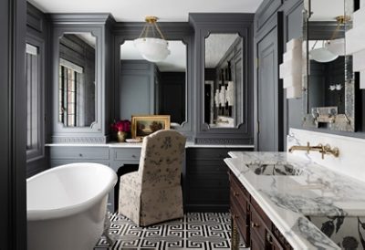 A luxurious gray bathroom with a white bathtub, marble double vanity, ornate mirrors, and a geometric floor pattern with walls painted Roycroft Pewter. 