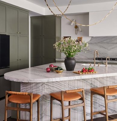 Modern kitchen with marble backsplash and island topped with vase of flowers and fresh vegetables, and Roycroft Bronze Green perimeter cabinets. 