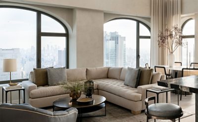 Modern living room with neutral color scheme, large windows, a beige sectional sofa, a dining table, and a marble kitchen island. 