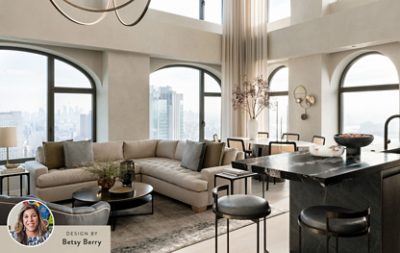 Modern living room with neutral color scheme, large windows, a beige sectional sofa, a dining table, and a marble kitchen island, with a headshot of designer Betsy Berry in the corner of the image.