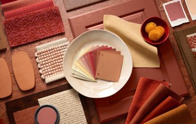 An arrangement of design materials featuring color swatches, fabric samples, and textured items in warm earth tones on a wooden surface. 