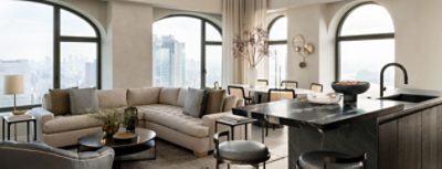 Modern living room with neutral color scheme, large windows, a beige sectional sofa, a dining table, and a marble kitchen island. 