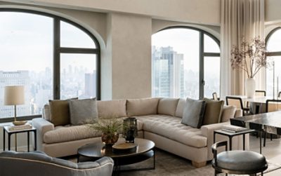 Modern living room with neutral color scheme, large windows, a beige sectional sofa, a dining table, and a marble kitchen island. 