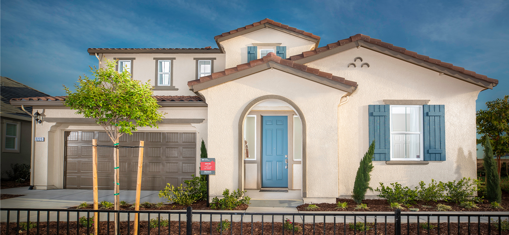 Spanish-style modern home exterior with beige stucco, attached garage, and arched entryway with blue entry door and shutters.