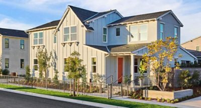 Angle shot of gray home exterior with dark orange front door and fence bordering sidewalk.