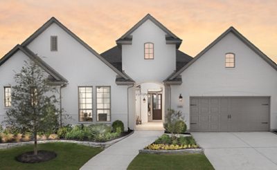 Street view of new home painted white with steep gables, attached garage, and lush landscaping at sunset.