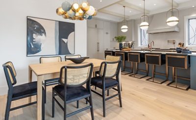 Open concept kitchen and dining area with modern light fixtures, leaded glass, and blue-green island.