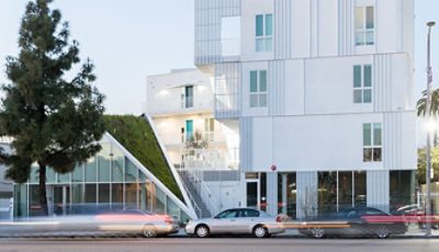Exterior shot of white modern four-story apartment building with wedge of green space extending down from the roof to street level.