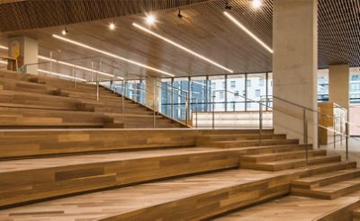 Wide wooden stairway inside a modern office space with stair steps at right and tiered stadium bench seating at left.