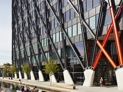 Exterior of the Brunel Building shown close up at ground level, where the supports of the steelwork exoskeleton can be seen reaching up to the rest of the structure, out of frame.