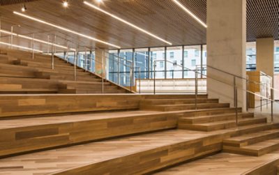Wide wooden stairway inside a modern office space with stair steps at right and tiered stadium bench seating at left.