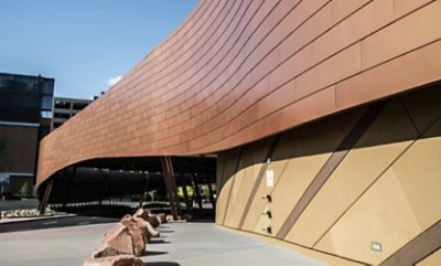 Another angle of the T-Mobile Arena, showing an entrance with copper-colored curved panels and metal supporting columns. 