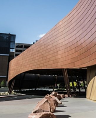 Another angle of the T-Mobile Arena, showing an entrance with copper-colored curved panels and metal supporting columns. 