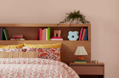 Bedroom painted in SW 6610 Koral Kicks, with wooden bookshelf behind the bed with a printed bedspread.