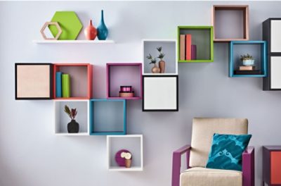 A chair against a wall with many square floating shelves painted bright colors.