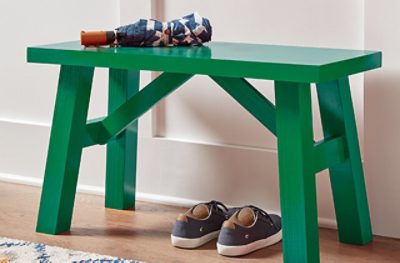 A green bench with an umbrella sitting on top of it and a pair of shoes below.