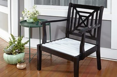 A brown wooden chair next to a small circular green table with a plant on it and 2 potted plants on the ground.