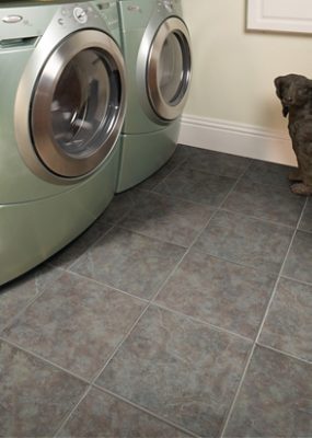 A laundry room with a new light green washer and dryer, dog statue and tile flooring.