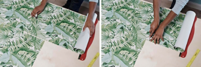 A person lines up strips of green tropical leaf wallpaper and cuts it to size.