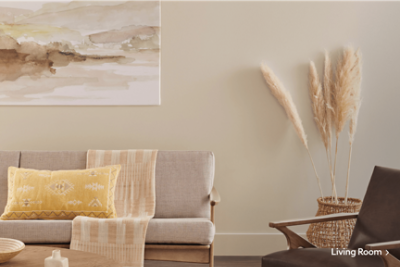 A living room with tan furniture and walls with a yellow accent pillow on a sofa.