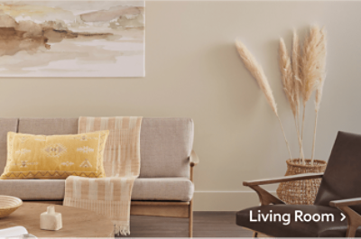 A living room with tan furniture and walls with a yellow accent pillow on a sofa.