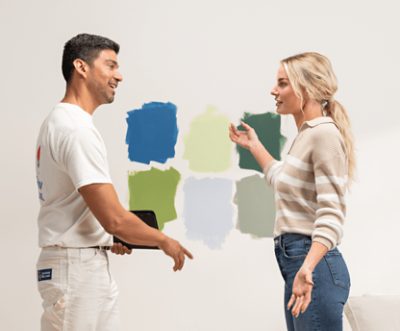 Two people talking in front of a wall with six different paint color samples.