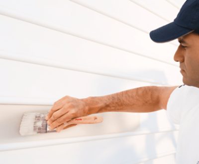 A person painting exterior siding with a paint brush.