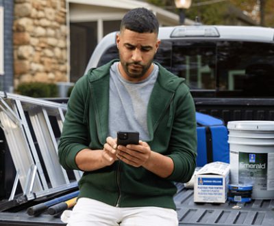 A person sitting in the back of a truck on his phone with paint supplies in the background.