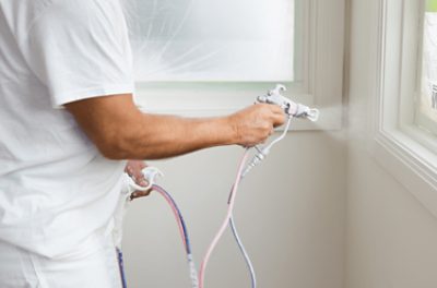 A person painting window sills with a sprayer.