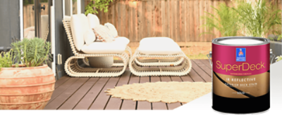 A deck stained a dark red-brown with potted plants, a circular outdoor rug and white modern furniture and a can of SuperDeck.