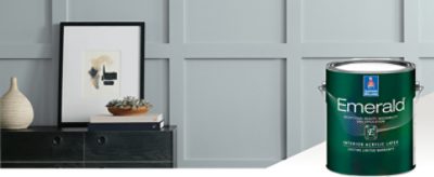 A wall painted light gray with a black side table with decor and a can of Emerald interior paint.