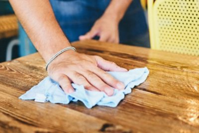 Close-up of a person's hand using a cloth to clean a wooden surface.