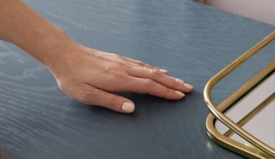 Close-up of a person's hand gently touching a dark wood-stained table.