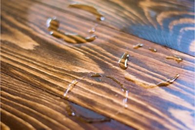 Close-up of a wooden table with light and dark brown tones, showing three circular wet water spots left by drinking glasses.