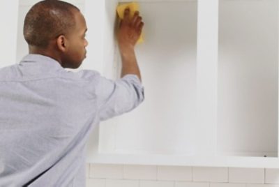 A person cleaning the inside of an empty wall cabinet with a sponge.