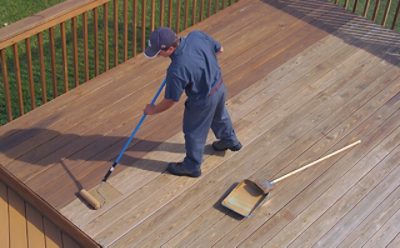 A man staining an exterior deck with a paint roller. 