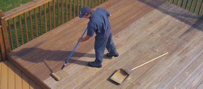 A man staining an exterior deck with a paint roller. 