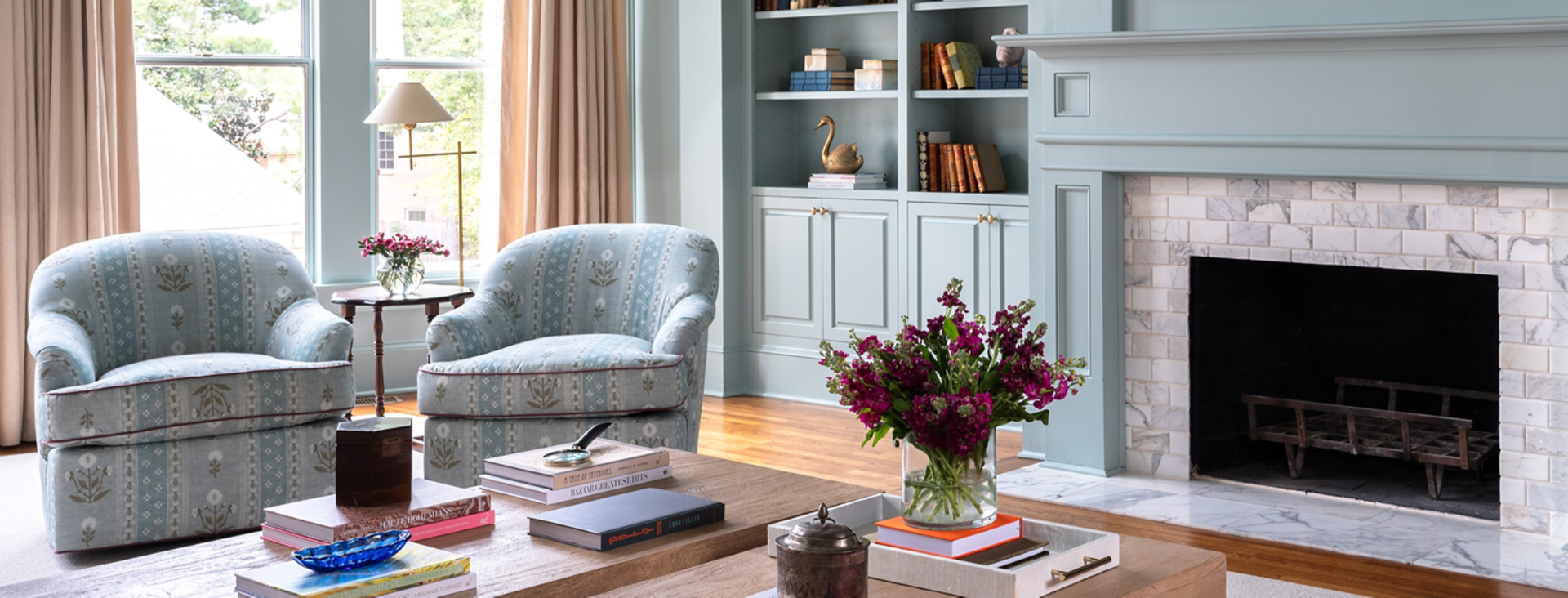 Light blue-green painted living room with matching round back arm chairs near tiled fireplace.