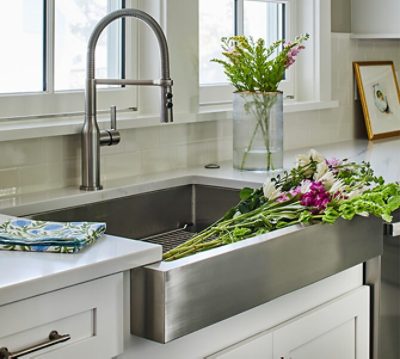 A large stainless steel farmhouse sink full of fresh-cut flowers ready to be arranged in a glass vase.